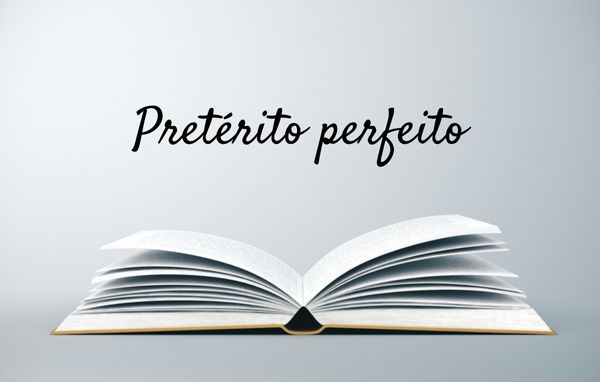 Livro aberto abaixo do escrito “pretérito perfeito”.