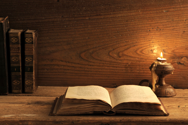 Livro antigo sobre uma mesa de madeira iluminada pela luz de uma vela, representando a ideia de “estilos de época”.